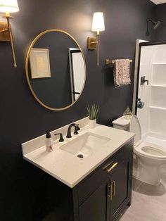 a white toilet sitting next to a bathroom sink under a round mirror on a wall