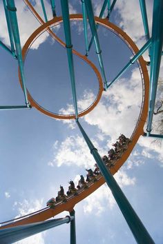 an amusement park ride with people on it's roller coaster and clouds in the background