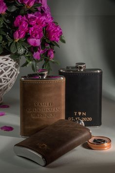 two flasks and a leather wallet on a table with flowers in the background