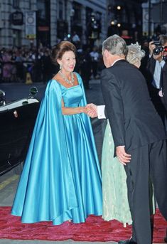 an older man and woman in formal wear shake hands on a red carpeted area