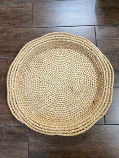 a round woven placemat on the floor in front of a wood flooring surface