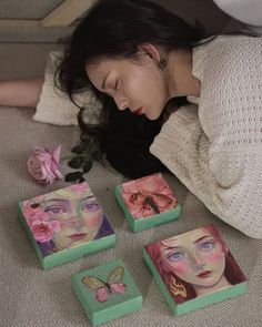 a woman laying on top of a bed next to four small boxes with paintings on them