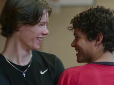 two young men are laughing together in the gym, one is wearing a red shirt and the other has a black t - shirt