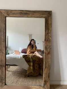 a woman sitting on top of a bed while talking on a cell phone in front of a mirror