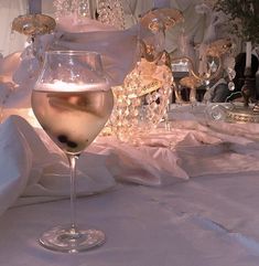 a glass of wine sitting on top of a white table cloth covered table with chandeliers in the background