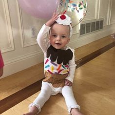 a baby is sitting on the floor with balloons in front of her and wearing a birthday hat