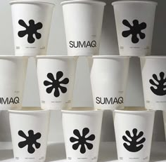 many cups with black designs on them are lined up against a white wall and have the words sumag printed on them