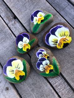 four painted rocks sitting on top of a wooden table next to each other with flowers in them