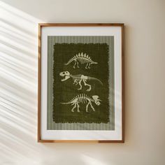 an image of a dinosaur cross stitch pattern in a frame on the wall with sunlight streaming through it