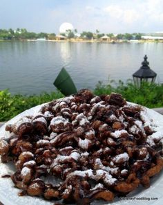 a white plate topped with lots of powdered sugar covered food next to a body of water