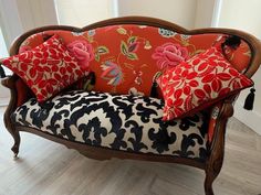 an ornate couch with red and black pillows on it's back, in front of a window