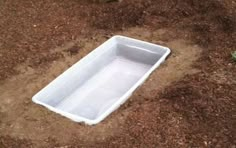 an empty white plastic container sitting on the ground in dirt and mulchy area