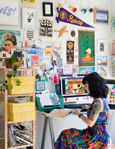 a woman sitting at a desk with lots of art on the wall behind her and writing