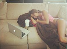 a woman is sleeping on the couch with her laptop and cup in front of her