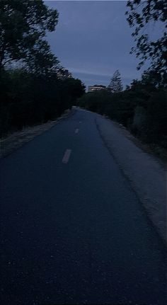 an empty street at night with trees on both sides and dark sky in the background