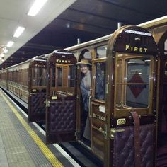 people standing on the side of a train at a station with its doors open and one person inside