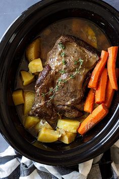 a pot roast with potatoes, carrots and meat in it on a table cloth