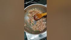 a pan filled with rice and vegetables on top of a stove next to a wooden spoon