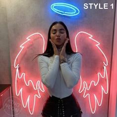 a woman standing in front of a neon sign with an angel wings on it's back