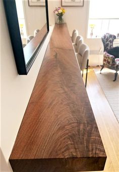 a long wooden table with chairs in the background and a mirror on the wall above it