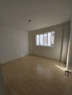 an empty room with hard wood flooring and large windows in the corner, all white walls