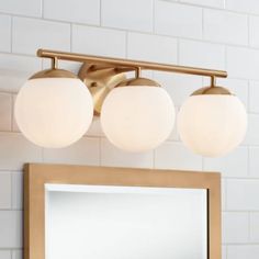 three globe lights are hanging on the wall above a mirror in a white tiled bathroom