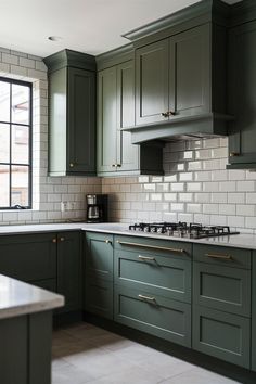 a kitchen with green cabinets and white tile backsplash, along with a window