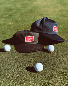 two hats sitting on top of a green field next to three golf balls in the grass