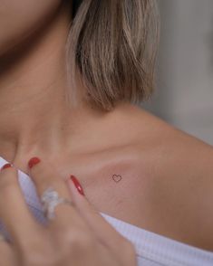 a close up of a woman's chest with a small heart tattoo on it