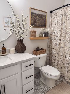 a white toilet sitting next to a sink in a bathroom under a mirror and a shower curtain