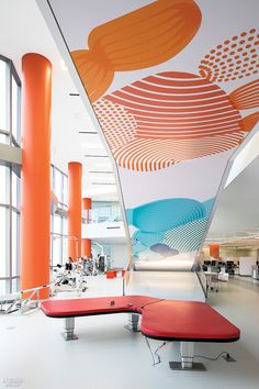 the interior of an office building with orange and blue accents on the ceiling, along with red benches