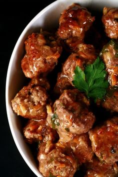 a white bowl filled with meatballs covered in sauce and garnished with parsley