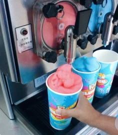 two cups of ice cream are being filled with blue and pink liquid in front of an espresso machine