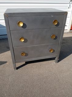 a gray dresser with gold knobs in front of a white building