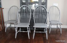 three white chairs sitting next to each other on top of a hard wood floor in front of a china cabinet