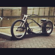 an old fashioned motorcycle parked on the side of a street next to a tree and water