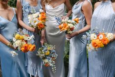 a group of bridesmaids in blue dresses holding bouquets with orange and white flowers