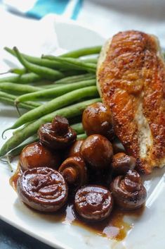 a white plate topped with meat, green beans and mushrooms next to some cooked veggies