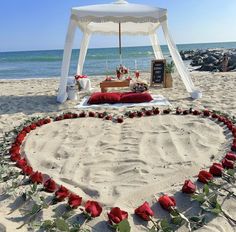 a heart - shaped bed on the beach with roses and petals arranged in the shape of a heart