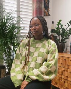 a woman with dreadlocks sitting in front of a window wearing a green and white sweater