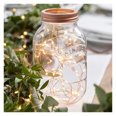 a mason jar filled with fairy lights sitting on top of a table next to greenery