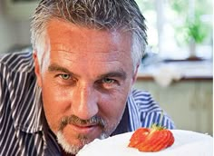 a man is holding a cake with strawberries on it and looking at the camera