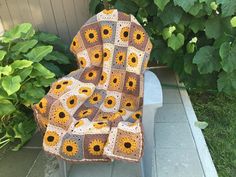 a crocheted blanket sitting on top of a chair in front of a bush