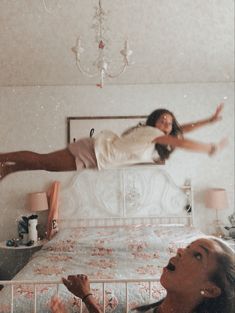 two women are laying on a bed and one is reaching up to the other side