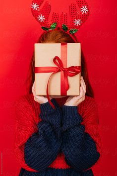 a woman with reindeer antlers on her head is holding a present in front of her face