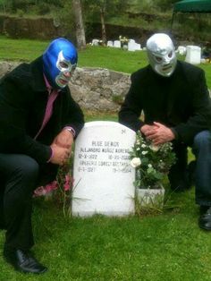 two people in masks sitting next to a grave