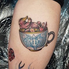 a tattoo on the leg of a woman holding a cup with an animal in it