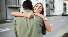 a man and woman embracing each other on the side of a road with apartment buildings in the background