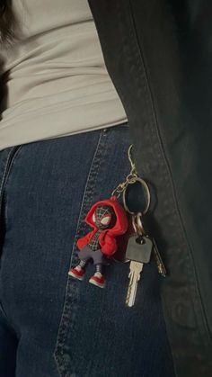 a person wearing jeans with a red keychain attached to their waist and holding two keys