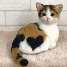 a stuffed cat sitting on top of a white blanket next to a brick wall with a black heart painted on it's chest